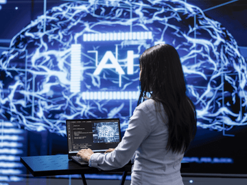 Mujer con un ordenador y una pantalla grande trabajando con inteligencia artificial